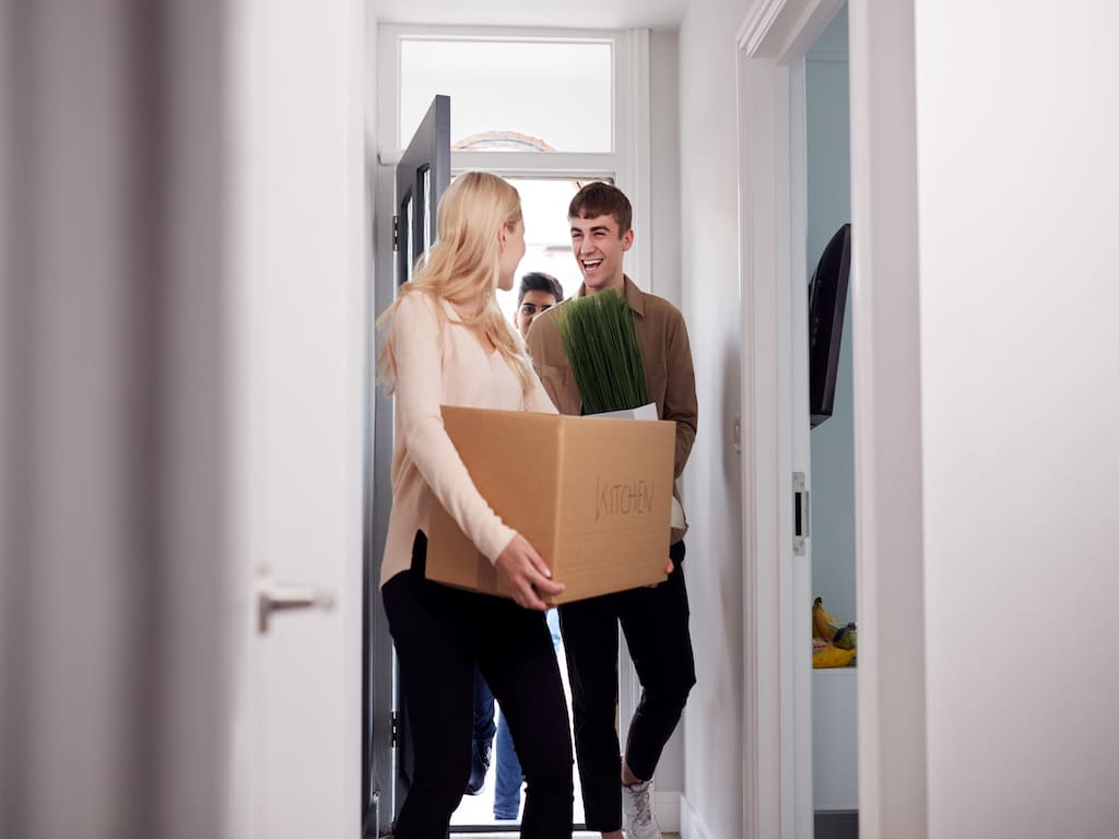 Group of college students carrying moving boxes into a living space together.