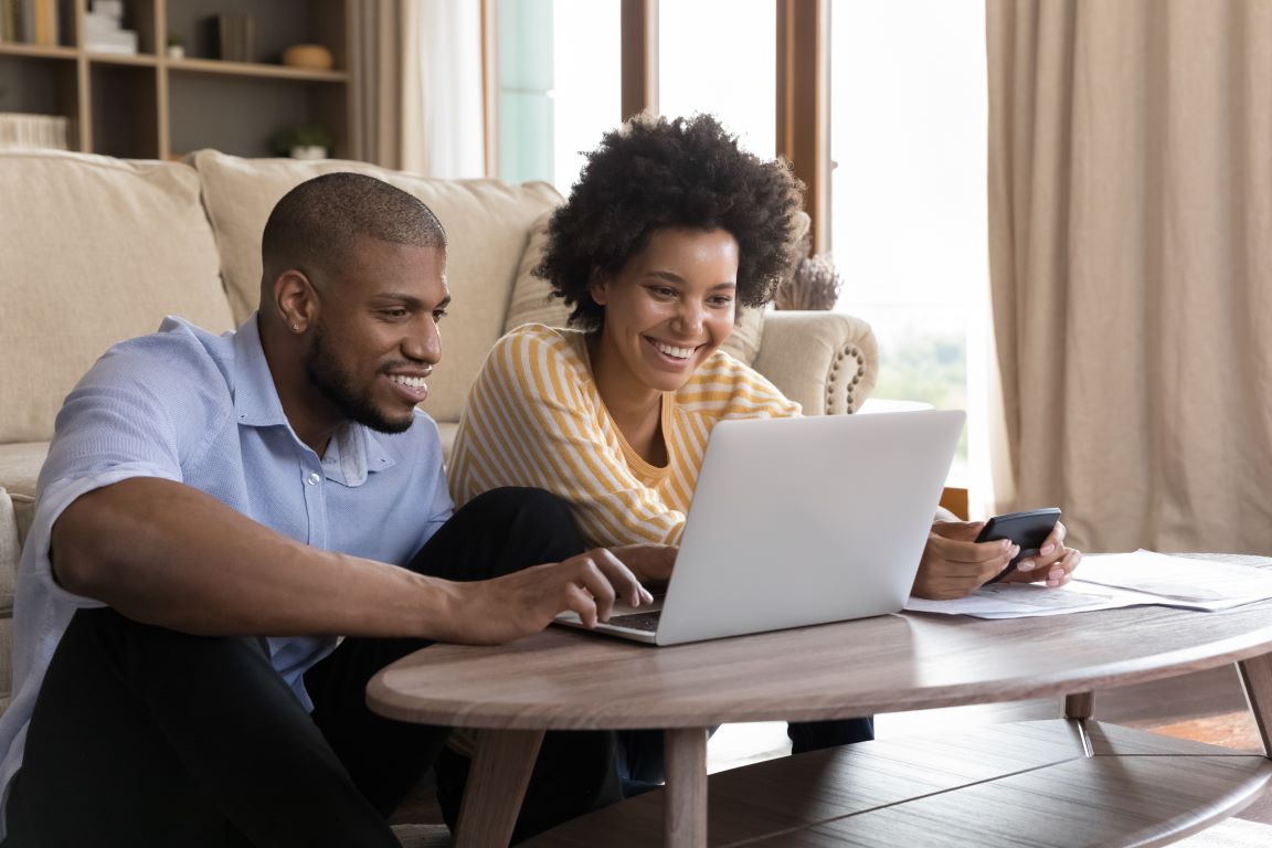 Man and woman looking at an open laptop on a coffee table and smiling.